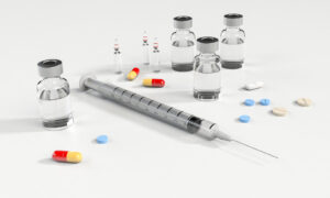 Verschiedene Medikamente in Pillenform, Kapseln, Ampullen mit Impfdosen und eine Spritze.